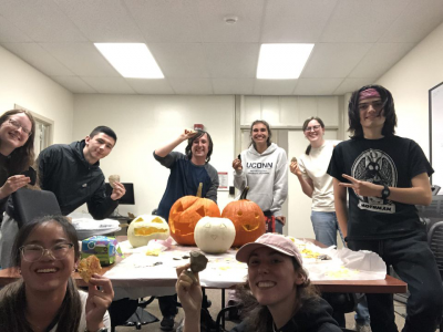 Several students from UConn Anthropology Club posing with stone tools around their carved pumpkins